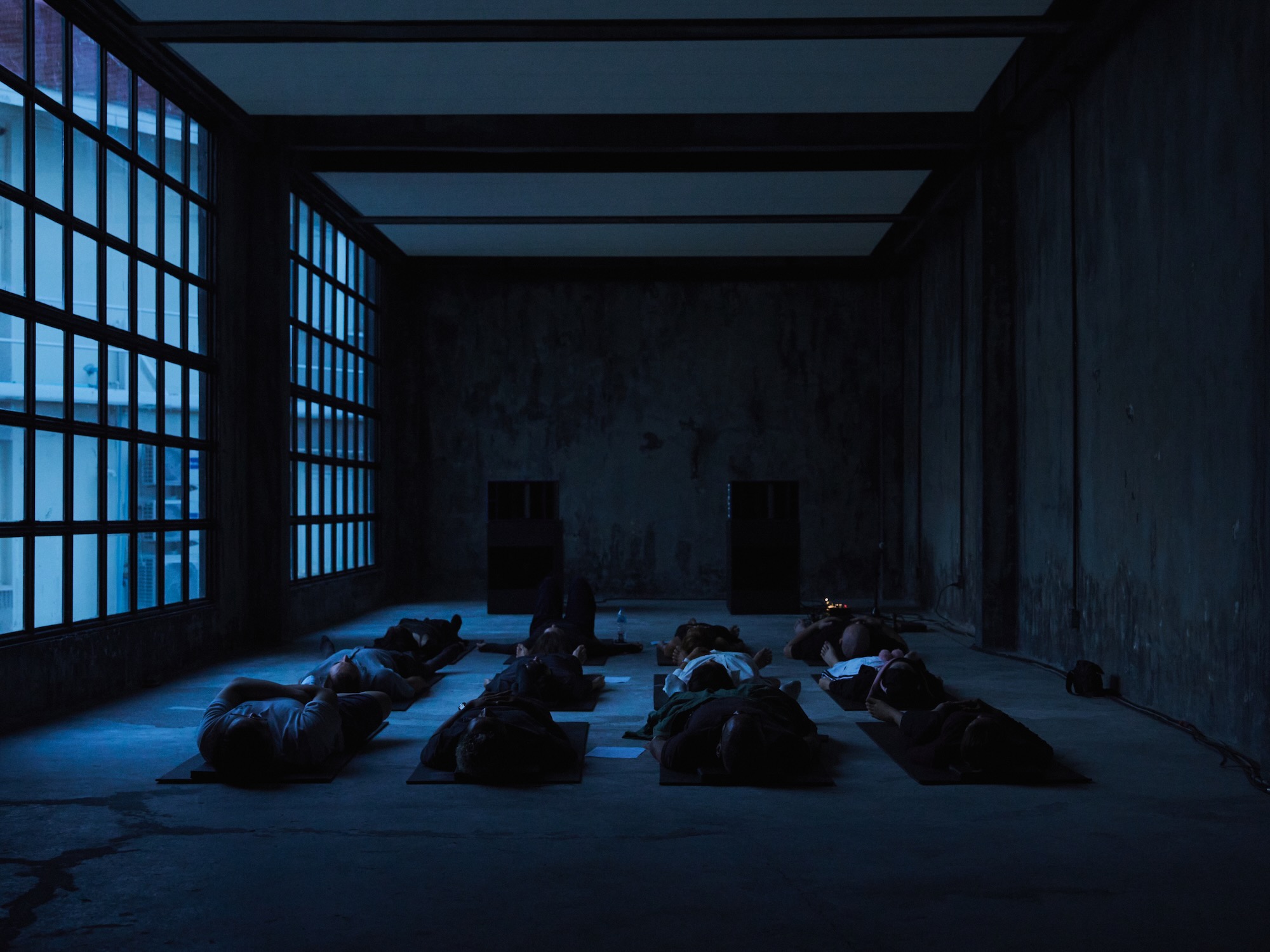People lying on mats in a dim hall during a Hardcore Yoga Nidra session